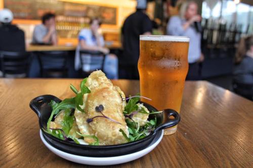 A plate of crispy fried food on a table next to a glass of beer, with a blurred background of people in a bar.