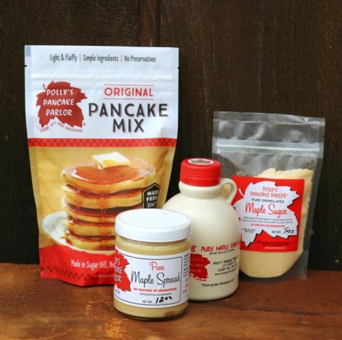 A collection of pancake mix, maple syrup, and maple spread on a wooden surface, featuring Polly's Pancake Parlor branding.