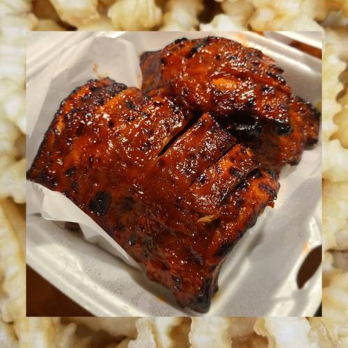 Grilled, glazed ribs on a serving tray, surrounded by a textured background of popcorn.