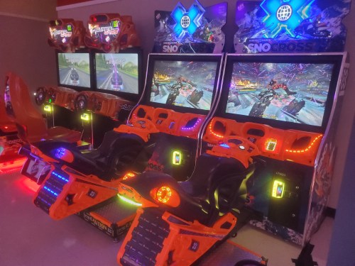 Two colorful arcade snowmobile racing games with large screens and illuminated controls in a gaming area.