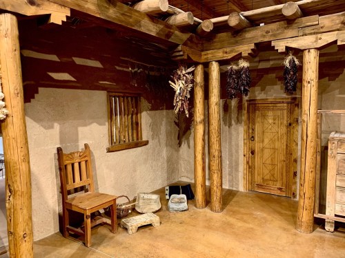 Interior of a rustic room with wooden beams, a chair, and dried herbs hanging from the ceiling. Warm, earthy tones.