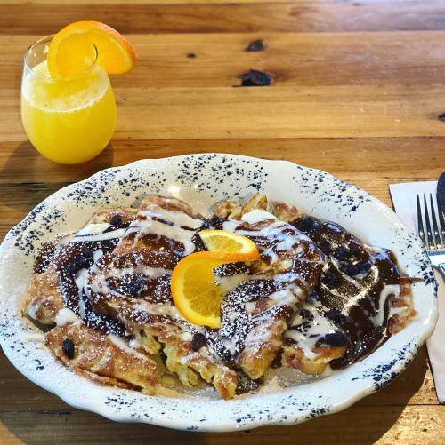 A plate of French toast topped with chocolate sauce, orange slices, and powdered sugar, alongside a glass of orange juice.