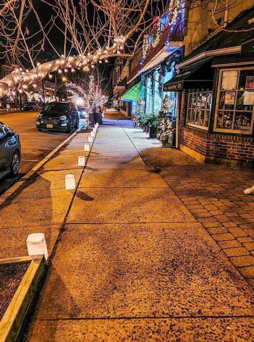 A charming street at night, lined with glowing lanterns and festive lights on nearby buildings and trees.