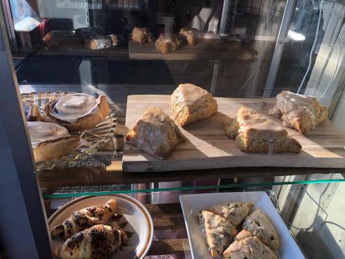 A display case with various baked goods, including scones, cinnamon rolls, and pastries on wooden and white plates.