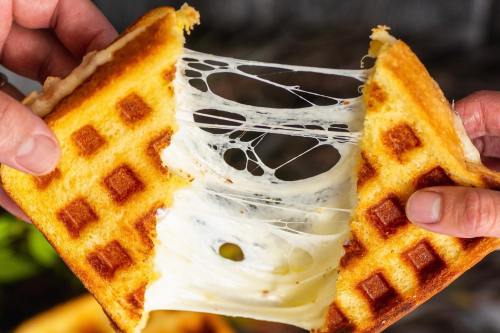 A person pulls apart a grilled cheese sandwich, revealing gooey, melted cheese stretching between the slices.