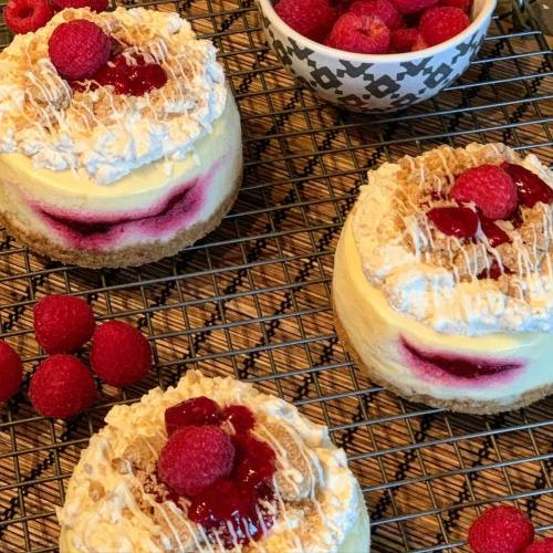 Delicious raspberry desserts topped with whipped cream and drizzled icing, surrounded by fresh raspberries on a cooling rack.