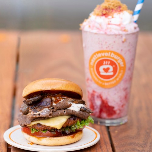 A stacked burger with lettuce, cheese, and sauce next to a tall milkshake topped with whipped cream and a straw.