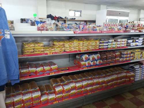 Shelves stocked with various brands of bread and baked goods in a store, with a few clothing items visible.