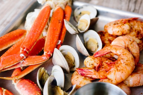 A metal tray filled with cooked shrimp, crab legs, and clams, showcasing a variety of seafood.