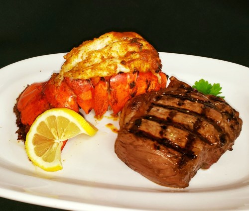 A plate featuring grilled lobster tail with a lemon wedge and a juicy steak, garnished with parsley.