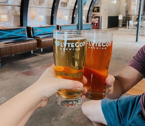 Two glasses of beer are clinking together in a brewery, with a cozy interior in the background.