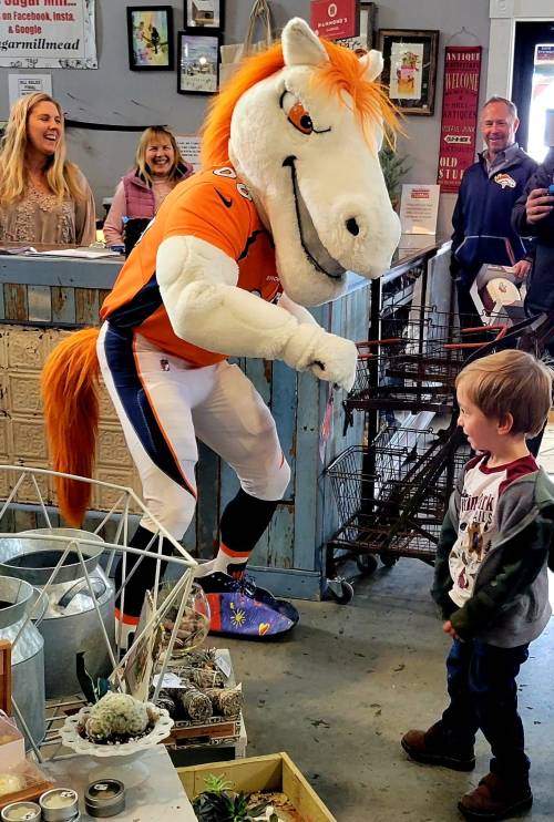 A costumed horse mascot interacts with a young child in a store, while adults watch and smile in the background.