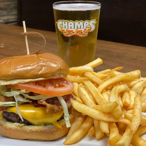 A juicy cheeseburger with bacon, lettuce, and tomato, served with fries and a pint of beer in the background.