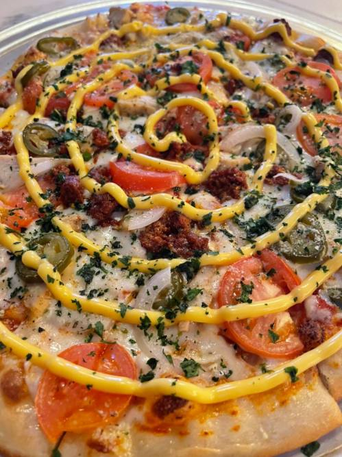 A close-up of a pizza topped with cheese, tomatoes, jalapeños, onions, and a spiral of yellow sauce.