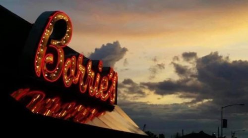 Neon sign reading "Barrie's" against a colorful sunset with clouds.