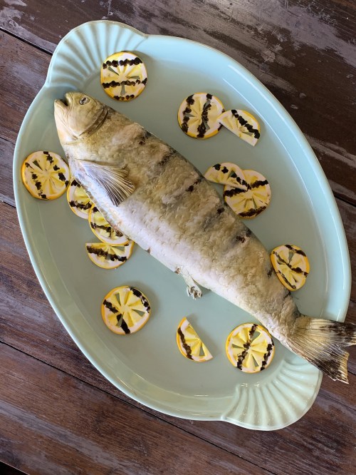 A whole fish on a light blue platter, surrounded by grilled lemon slices.