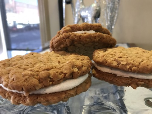 Three oatmeal cream pies on a reflective surface, with two pies stacked and one leaning against them.