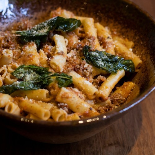 A bowl of pasta with meat sauce, topped with spinach and grated cheese, served in a rustic dish.