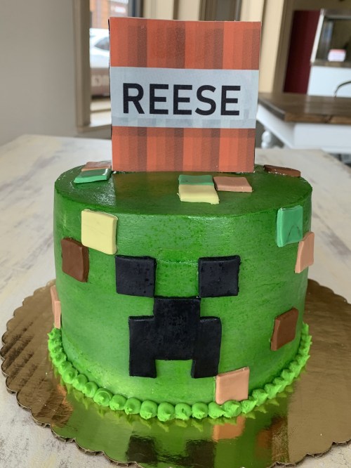 A green cake decorated with a pixelated design and a sign that reads "REESE" on top.