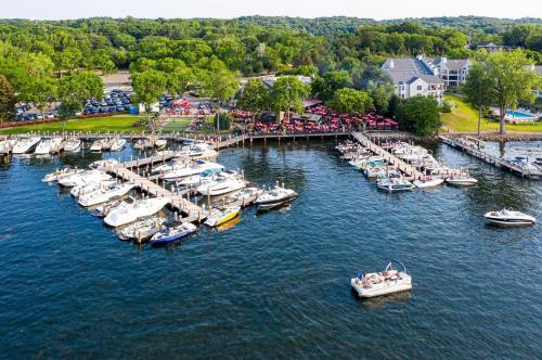 Aerial view of a busy marina with boats docked and people enjoying a waterfront restaurant in a lush green setting.
