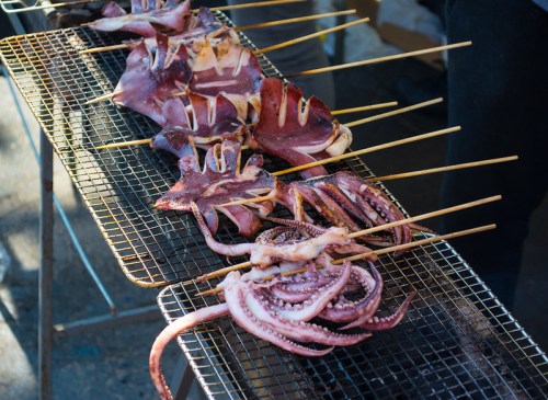 Grilled octopus and squid skewers on a metal grill, ready for serving at a street food market.