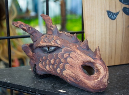 A detailed dragon mask with scales and spikes, displayed on a shelf against a blurred background.