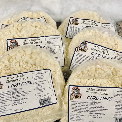 Several packages of white cheddar cheese curds labeled "Curd Fines," with nutrition facts and expiration dates visible.