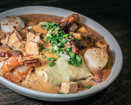 A bowl of creamy seafood and chicken dish with shrimp, scallops, and green onions on top.