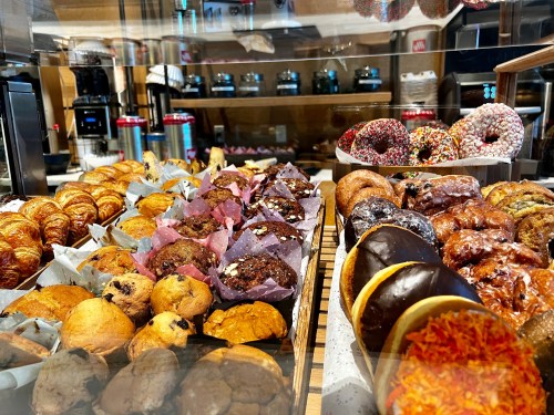 A display of assorted baked goods, including croissants, muffins, and colorful donuts in a bakery setting.
