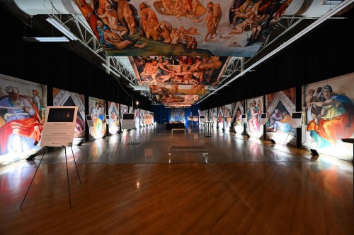 A spacious gallery featuring large murals on the ceiling and walls, illuminated displays, and a polished wooden floor.