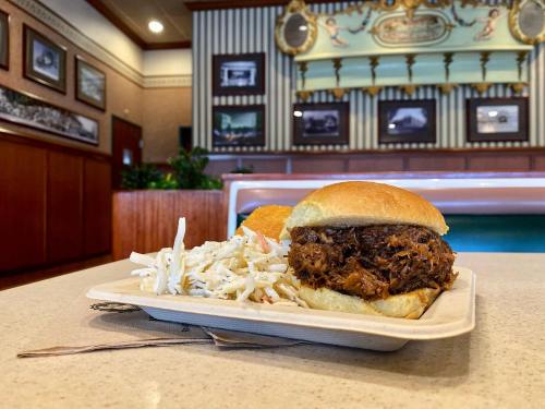 A pulled pork sandwich on a bun with coleslaw, served on a tray in a cozy restaurant setting.