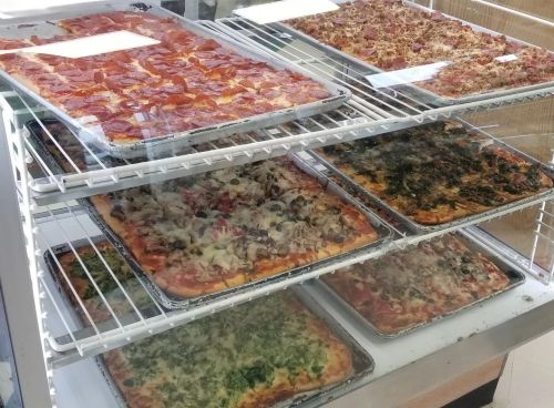 A display case filled with various types of pizza, including pepperoni, veggie, and meat toppings.