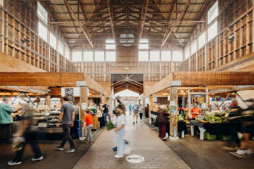 A bustling market interior with wooden beams, vendors, and shoppers moving through the aisles.