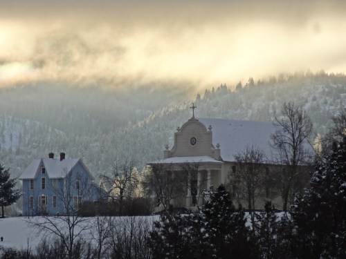 A snowy landscape featuring a blue house and a church, with misty mountains in the background.