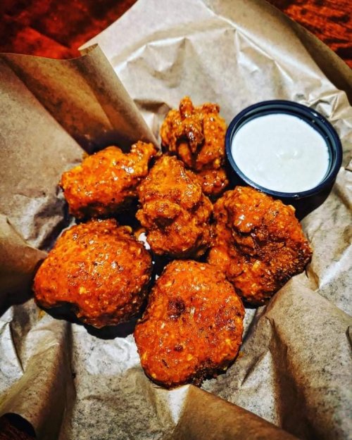 A serving of spicy chicken wings on parchment paper, accompanied by a small cup of creamy dipping sauce.