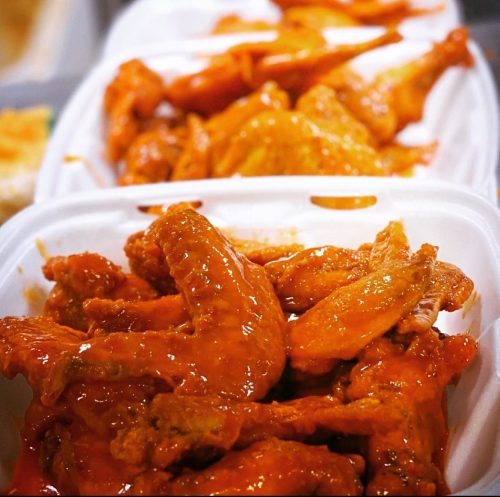 Close-up of saucy chicken wings piled in white takeout containers.