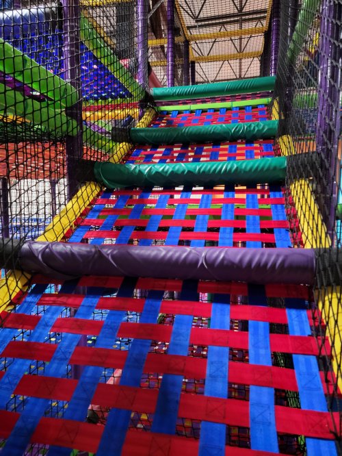 Colorful woven climbing structure in a play area, featuring red, blue, and green elements.