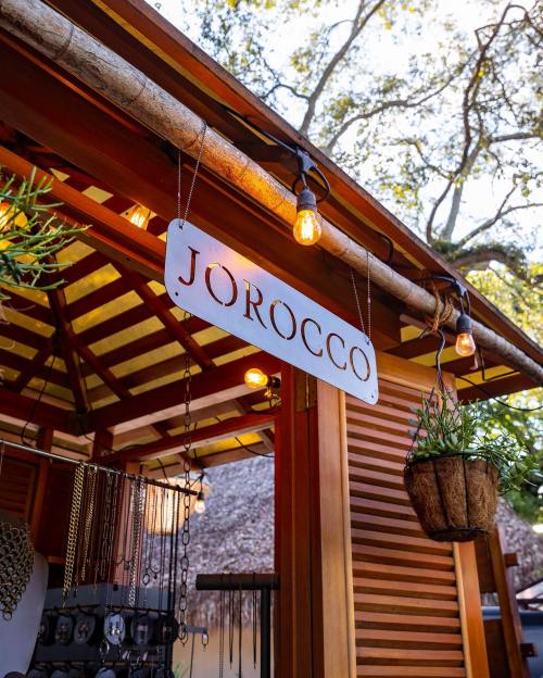A wooden stall with a sign reading "JOROCCO," adorned with hanging lights and plants.