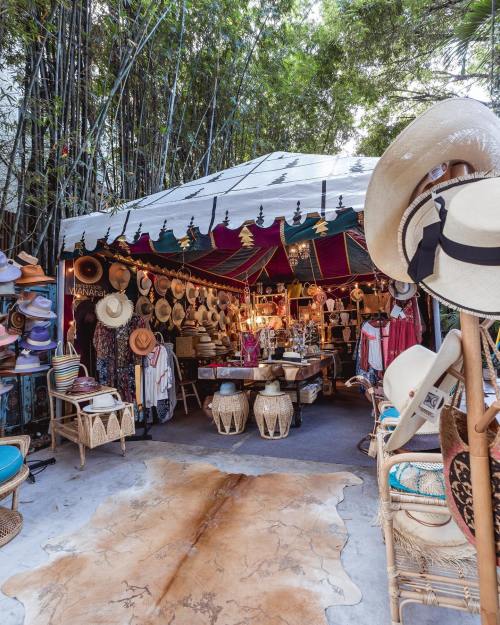A vibrant market stall filled with hats and accessories, surrounded by bamboo and decorated with colorful fabrics.