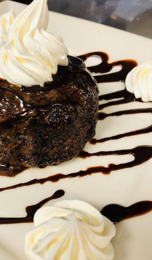 A rich chocolate dessert topped with whipped cream and drizzled with chocolate sauce on a white plate.