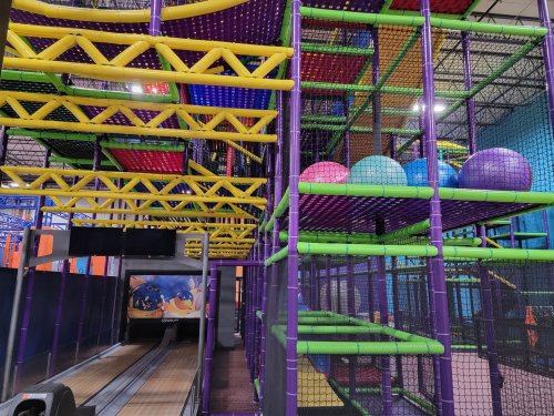 Colorful indoor play structure with climbing nets, slides, and large balls in a fun, vibrant environment.