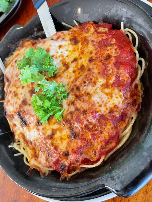 A serving of baked spaghetti topped with marinara sauce, melted cheese, and garnished with fresh parsley.