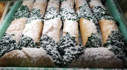 A tray of rolled pastries dusted with powdered sugar and topped with green sprinkles, resembling trees.