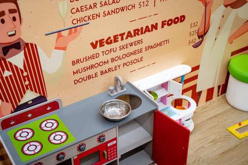 A colorful play kitchen setup with a toy stove, sink, and a menu featuring vegetarian food options on the wall.
