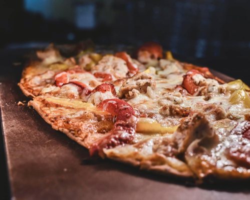 A close-up of a delicious pizza topped with cheese, chicken, and colorful vegetables, on a baking tray.
