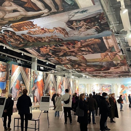 Visitors admire large-scale reproductions of Michelangelo's artwork in a modern gallery setting.