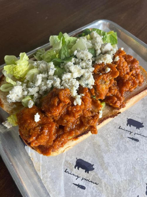 A sandwich with crispy chicken pieces coated in sauce, topped with lettuce and blue cheese on a toasted bun.