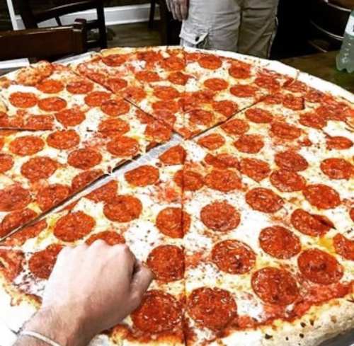 A large pepperoni pizza with multiple slices, placed on a table with a hand reaching for a slice.