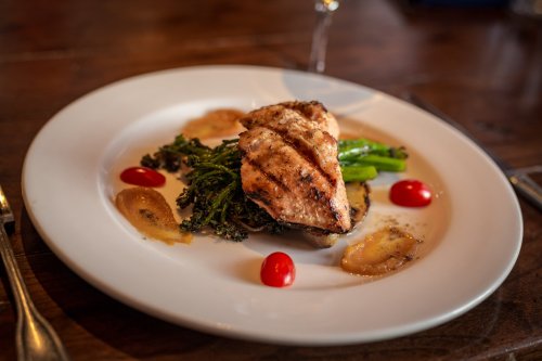 Grilled chicken breast on a bed of vegetables, garnished with cherry tomatoes and a drizzle of sauce on a white plate.