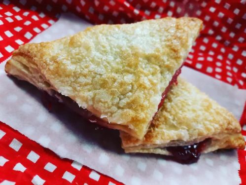 A golden, flaky pastry triangle filled with red fruit jam, resting on a red and white checkered cloth.